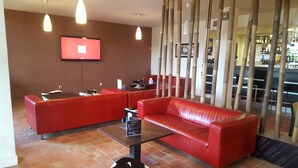 A modern lounge area with red leather sofas, a flat-screen TV mounted on the wall, and a bar in the background. - Hotel Mercure Aix en Provence Sainte Victoire (Chateauneuf-le-Rouge)