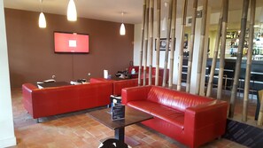 Uma área de convívio moderna com sofás de couro vermelho, uma TV de tela plana na parede e um bar ao fundo.