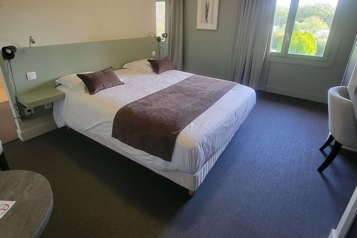 Une chambre d’hôtel avec un lit, une chaise, un bureau et une fenêtre avec des rideaux.