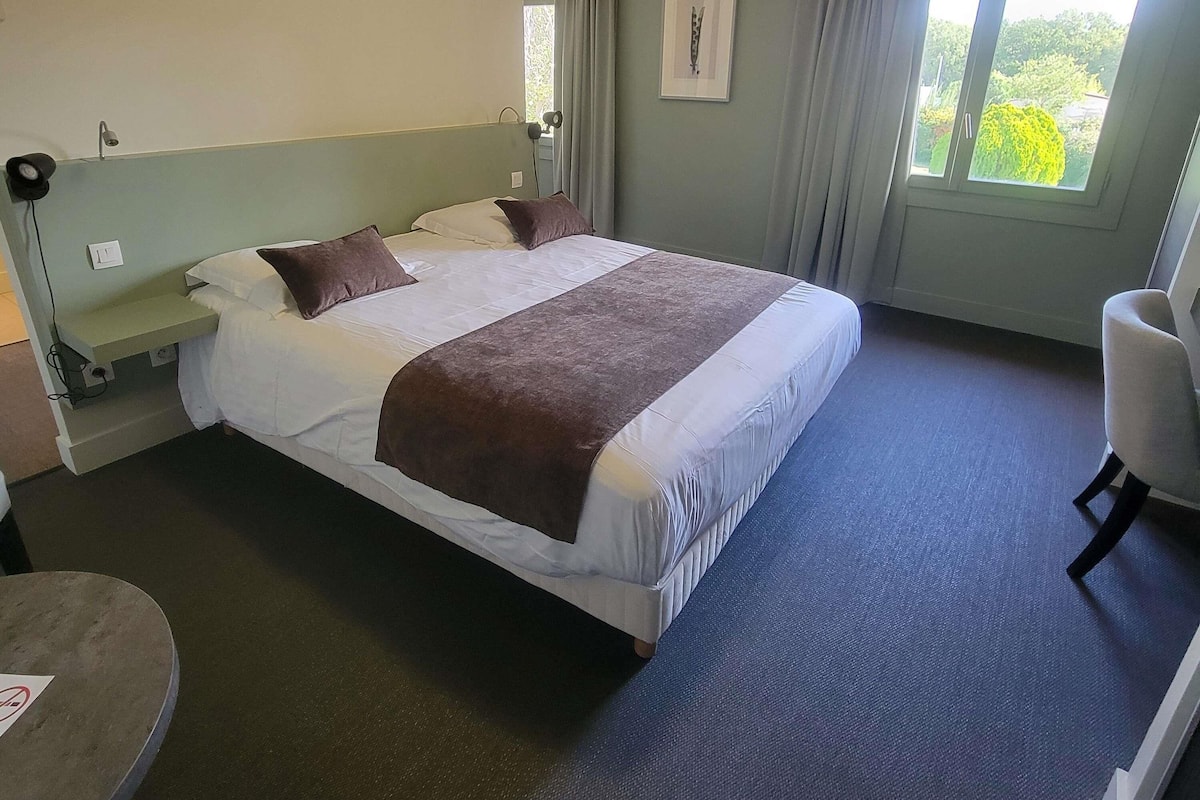 A hotel room with a bed, a chair, a desk, and a window with curtains.