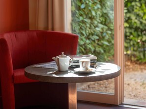 Une chaise rouge, une théière blanche et une tasse sur une table ronde, entourée de livres.