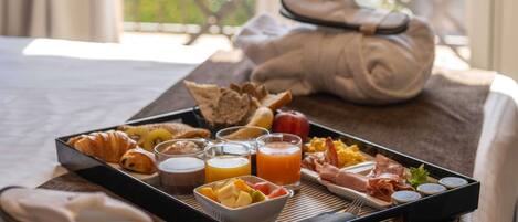 Un plateau de petit-déjeuner avec des croissants, des fruits, des œufs brouillés, du bacon et du jus, posé sur un lit.