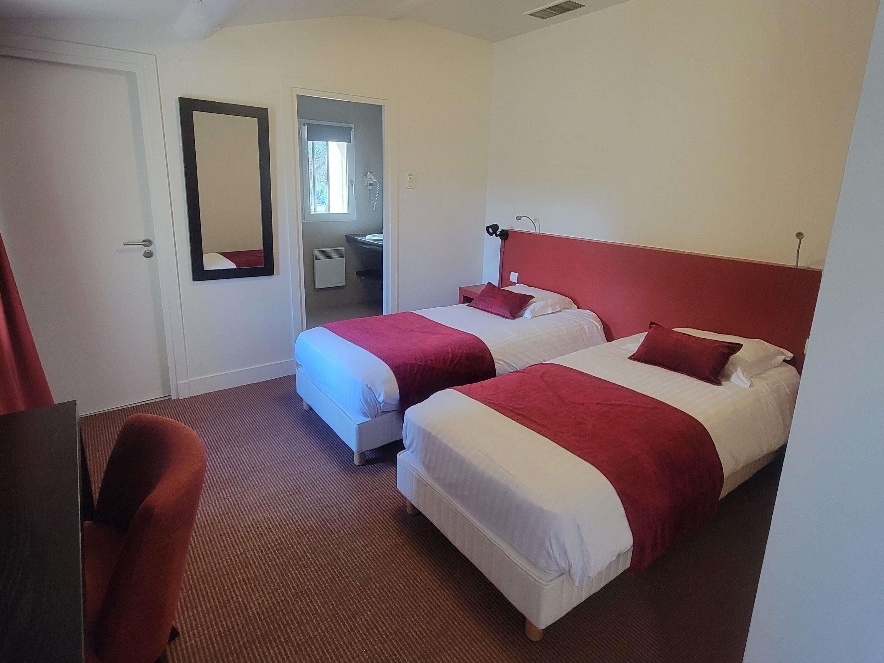 Habitación de hotel con dos camas, un escritorio, una silla, un espejo y un baño visible a través de una puerta abierta.