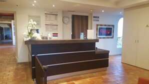 A reception desk with a dark wood finish, a clock, and informational signs on the wall. - Hotel Mercure Aix en Provence Sainte Victoire (Chateauneuf-le-Rouge)