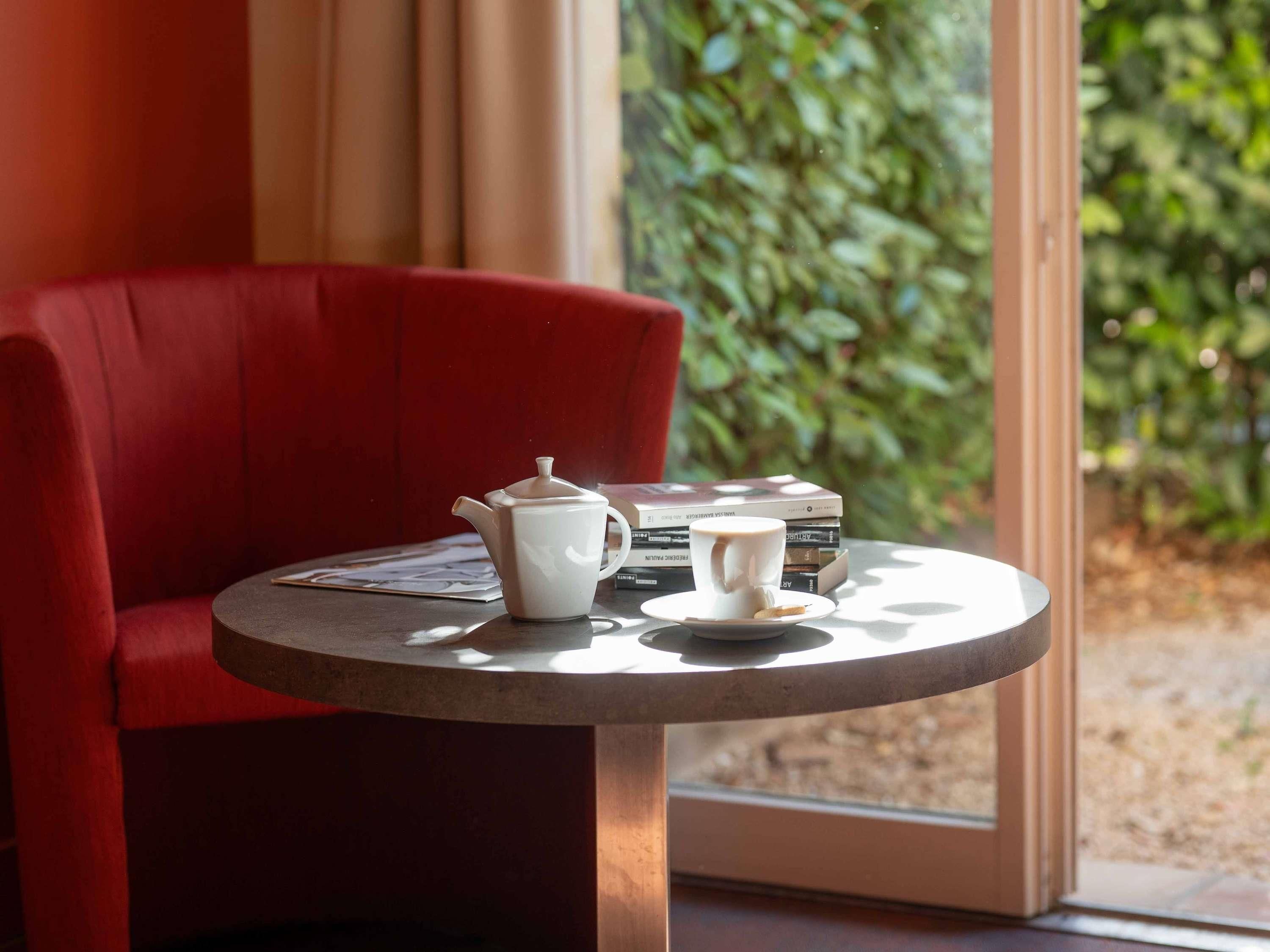 A red chair, a white teapot, and a cup on a round table with books.