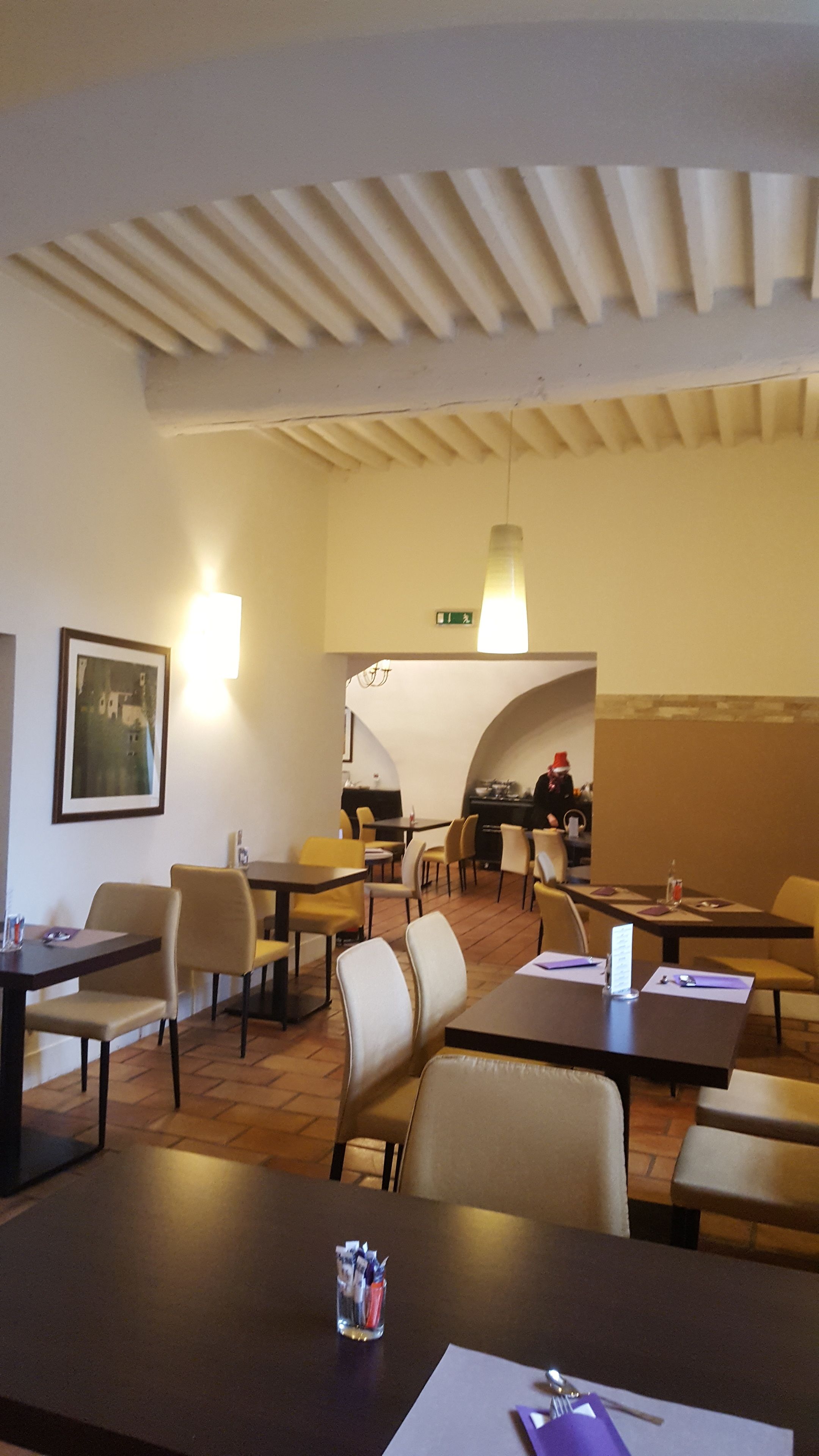 A hotel dining area with tables and chairs, a wall-mounted light, and a framed picture.