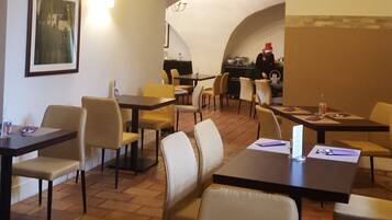 A hotel dining area with tables and chairs, a wall-mounted light, and a framed picture.