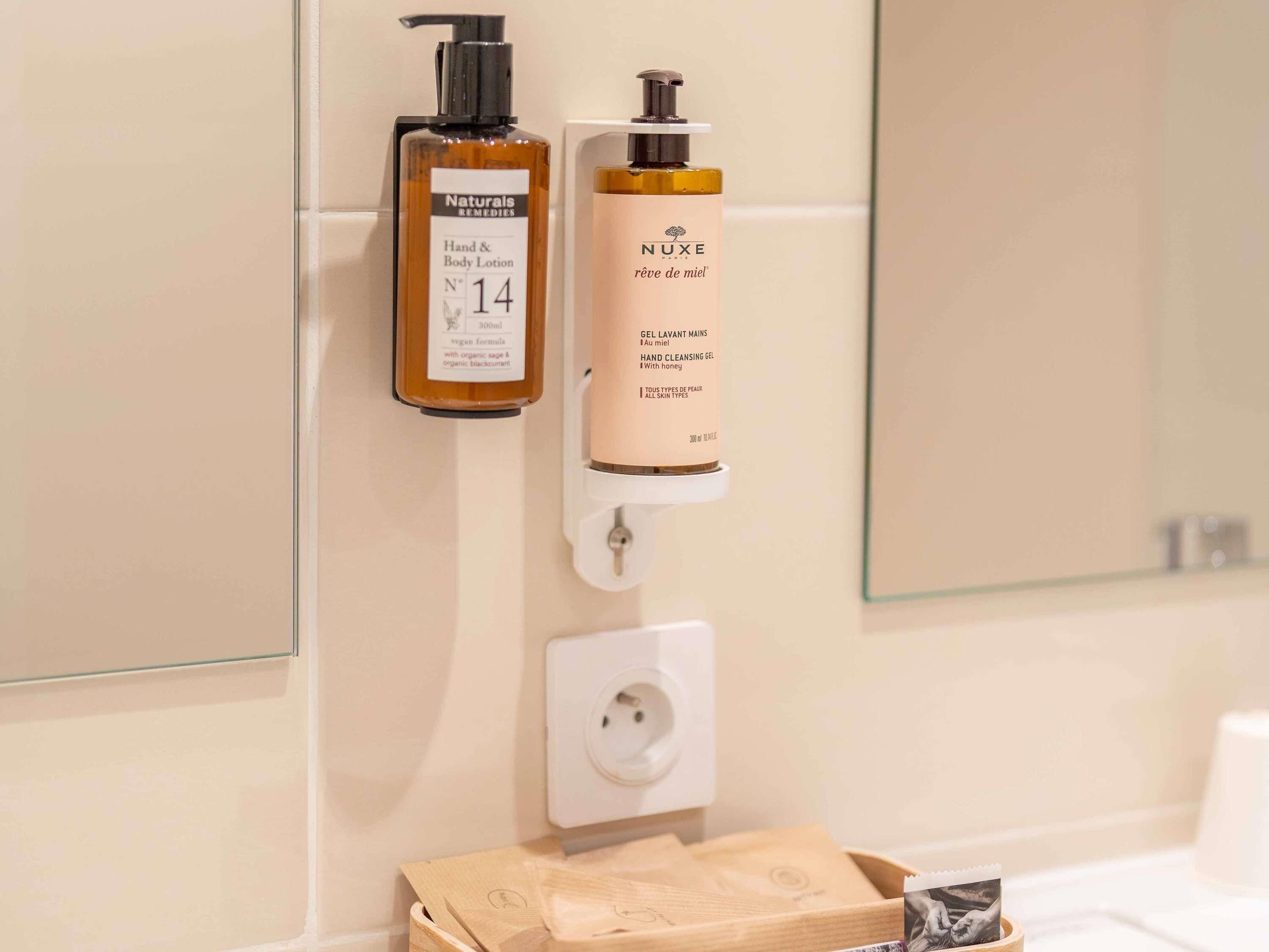Une salle de bain équipée de deux distributeurs de lotion pour les mains et le corps, d’un distributeur de gel hydroalcoolique et d’une boîte en bois contenant des mouchoirs.