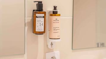 Une salle de bain équipée de deux distributeurs de lotion pour les mains et le corps, d’un distributeur de gel hydroalcoolique et d’une boîte en bois contenant des mouchoirs.
