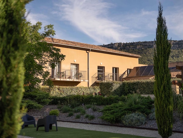 Un bâtiment doté d’un balcon, de panneaux solaires et d’un jardin agrémenté d’arbustes et d’une pelouse.