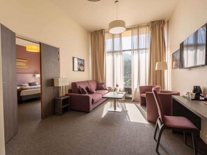 A hotel room with a sofa, armchair, desk, TV, and a bed with a view of the outdoors. - Hotel Mercure Aix en Provence Sainte Victoire (Chateauneuf-le-Rouge)