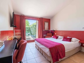 Hotelkamer met een bed, bureau, stoel, raam met gordijnen en uitzicht op groen.