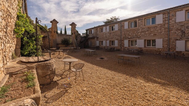 A courtyard with stone buildings, outdoor seating, and a gravel ground. - Hotel Mercure Aix en Provence Sainte Victoire (Chateauneuf-le-Rouge)