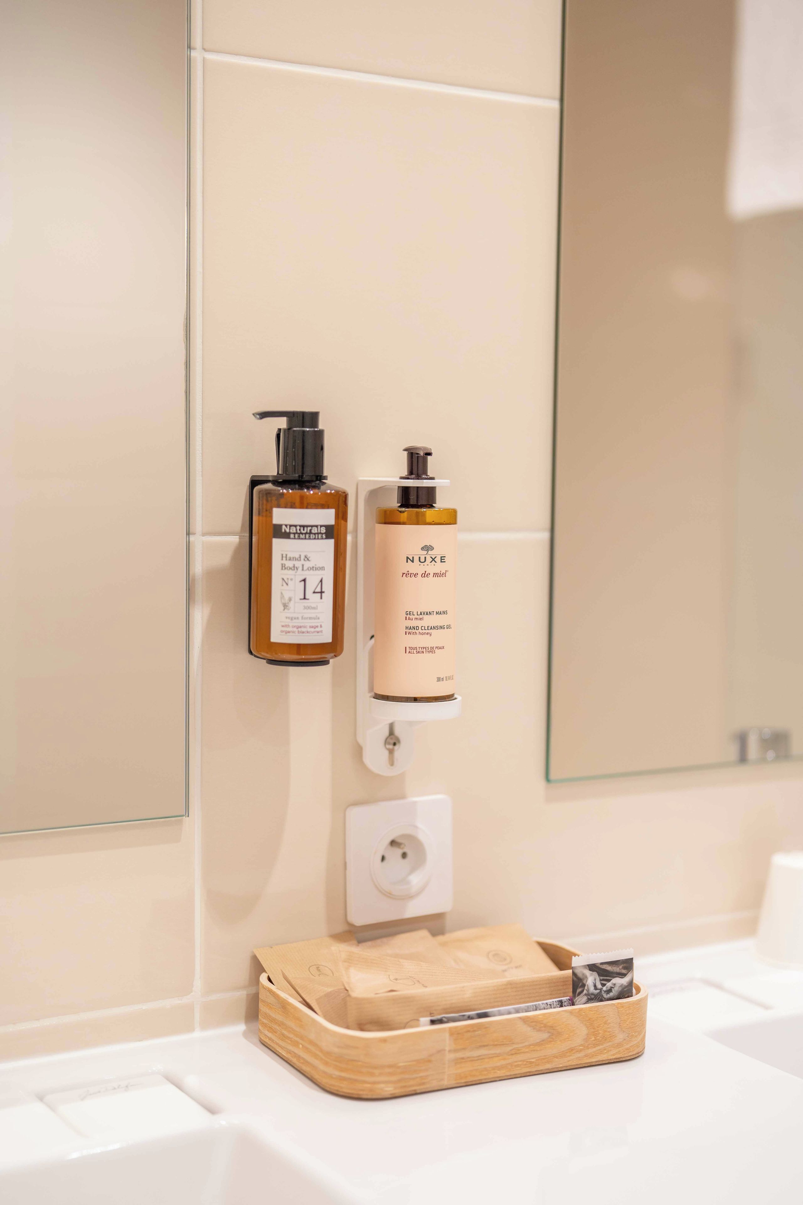 Un baño con dispensador de loción corporal, dispensador de gel limpiador de manos y una bandeja de madera con un marco de fotos sobre el mostrador.