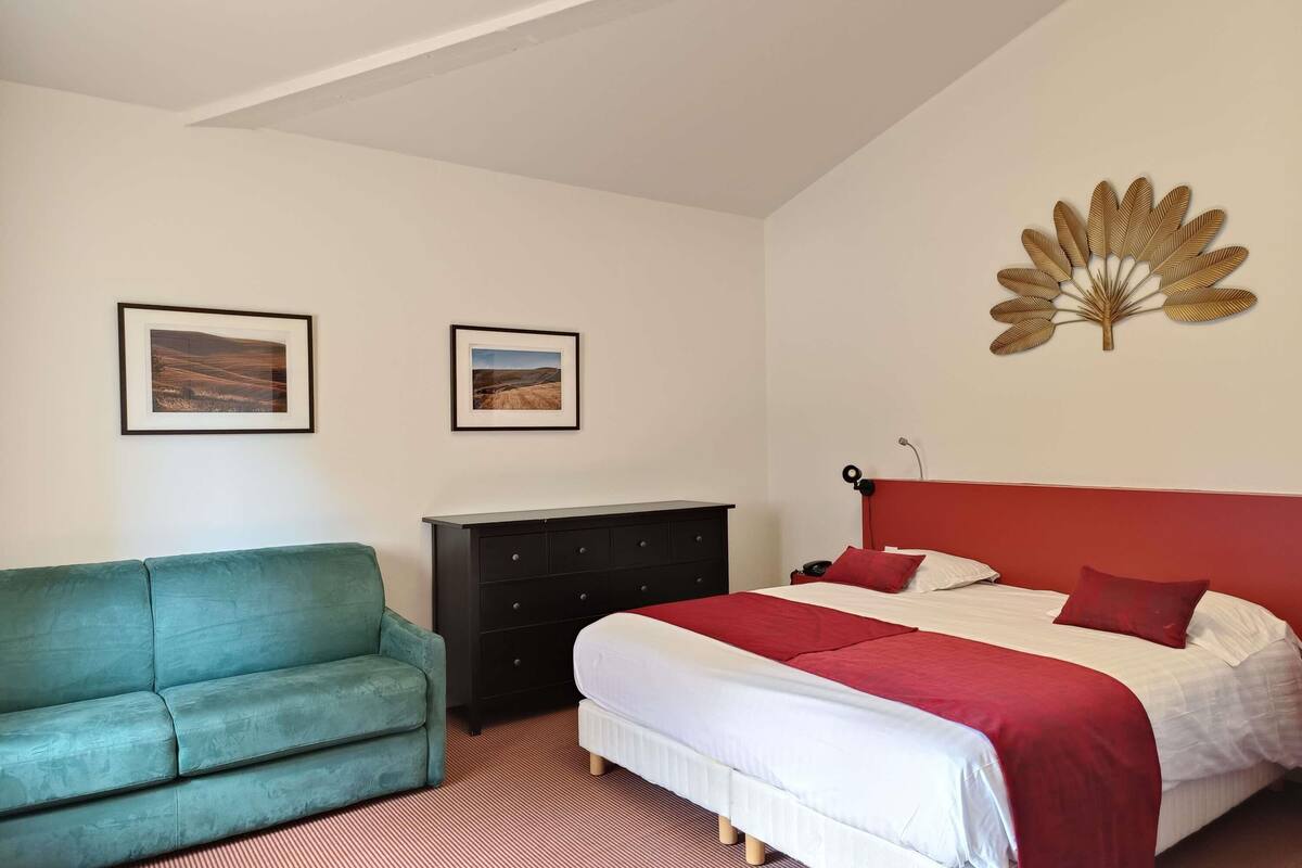 Une chambre à coucher avec un lit, une commode, un canapé vert et deux tableaux encadrés accrochés au mur.