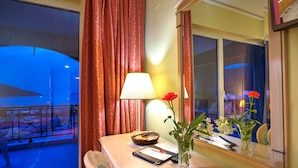 Habitación de hotel con escritorio, lámpara, un florero con flores y ventana con cortinas.