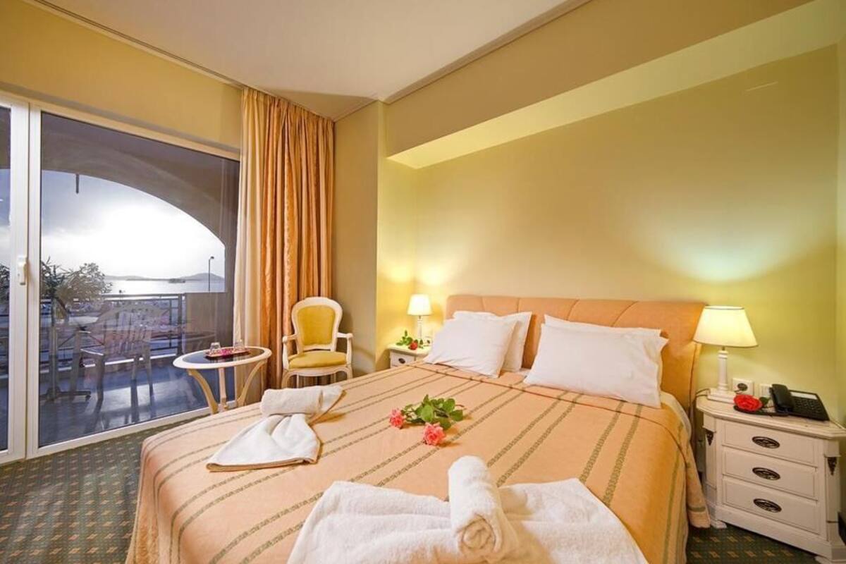 Une chambre d’hôtel comprenant un lit, une chaise, une petite table, un balcon, ainsi qu’une table de chevet avec une lampe et un téléphone.
