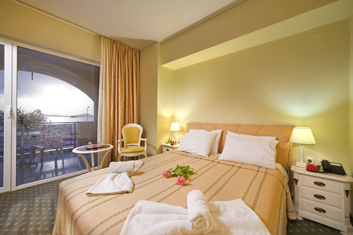 Une chambre d’hôtel comprenant un lit, une chaise, une petite table, une table de chevet et une vue sur l’extérieur grâce à une porte coulissante.