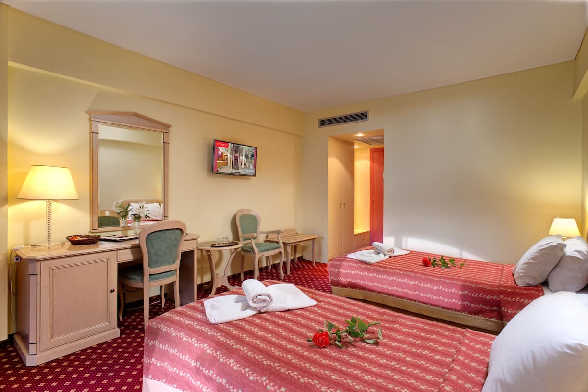 Une chambre d’hôtel avec deux lits, un bureau, une chaise, un miroir et une petite table.