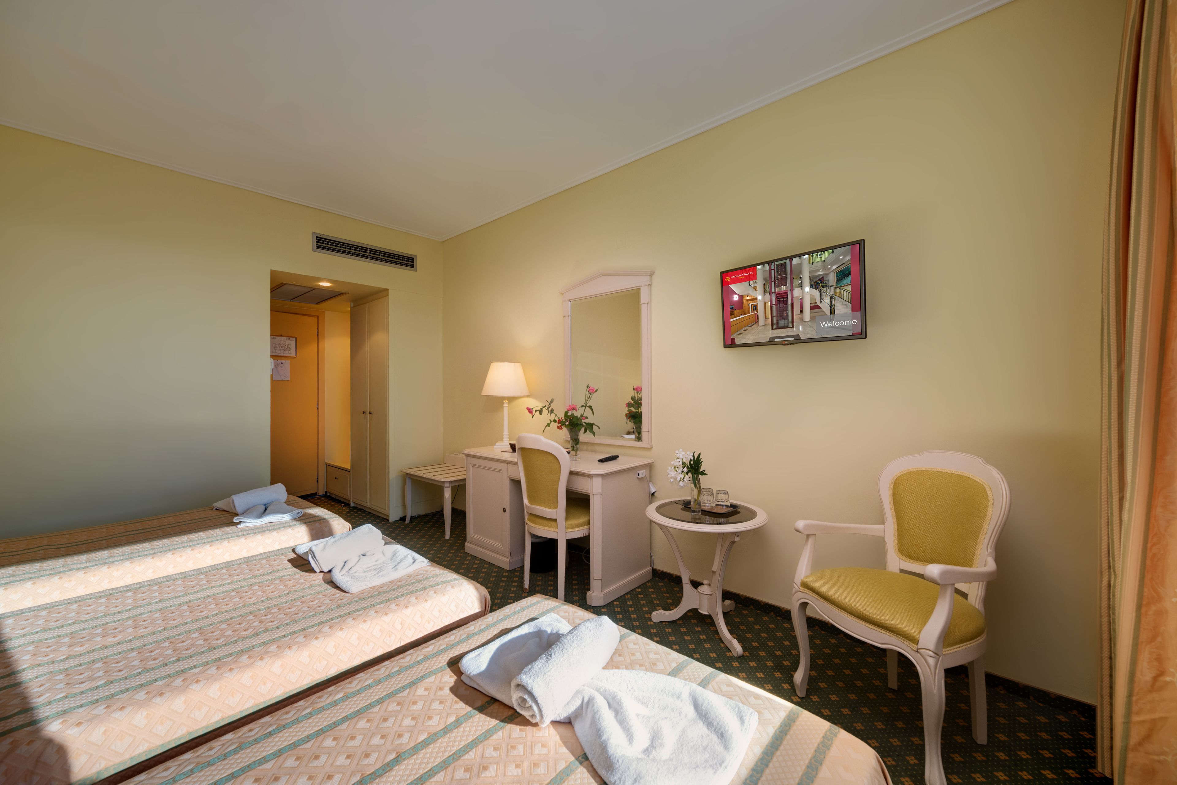 A hotel room with two beds, a desk, a chair, a small table, and a mirror.