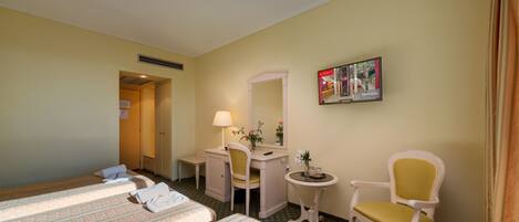 A hotel room with two beds, a desk, a chair, a small table, and a mirror.