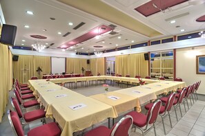 Un salón de conferencias con varias mesas y sillas, equipado con tarjetas de identificación y una pantalla para proyector.