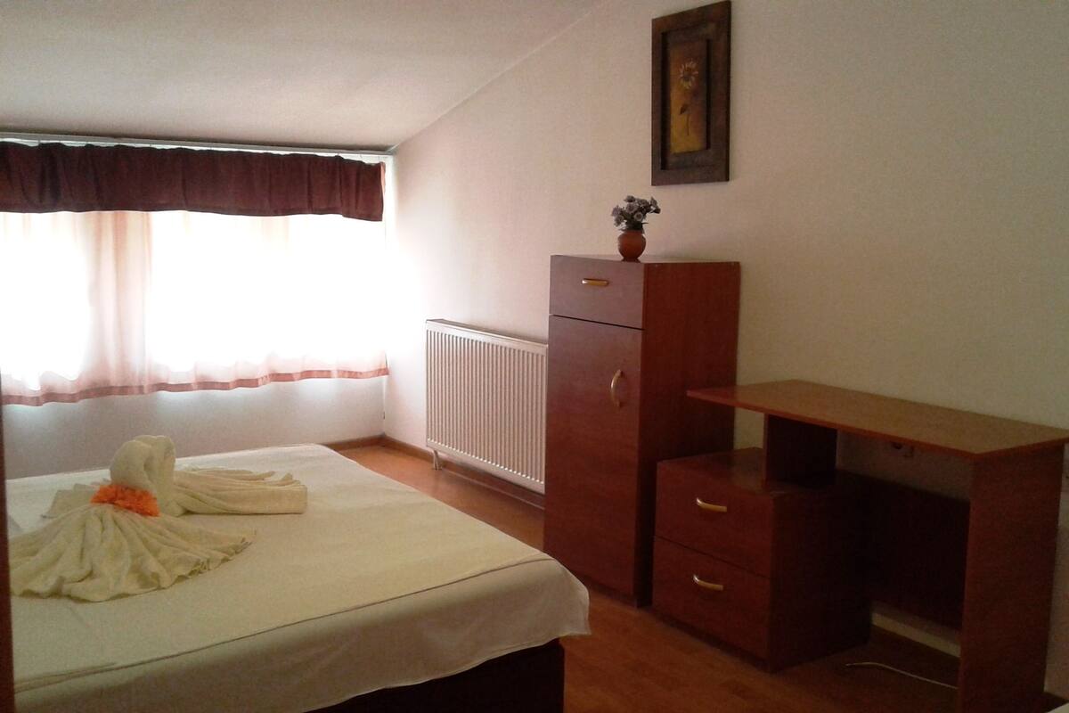 Un dormitorio con cama, cómoda, radiador y ventana con cortinas.