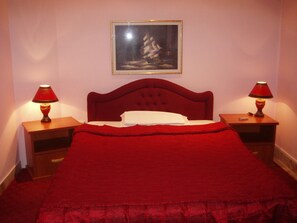 A bed with a red headboard, two bedside tables with lamps, a framed picture on the wall, and a red blanket. - Ani Hotel (Skopje)