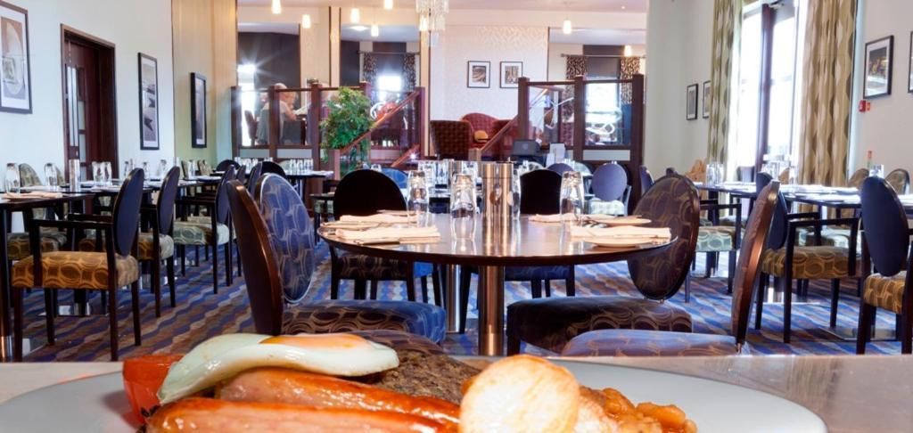 A hotel dining area with round tables, chairs, and a buffet table with food items.