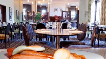 A hotel dining area with round tables, chairs, and a buffet table with food items.