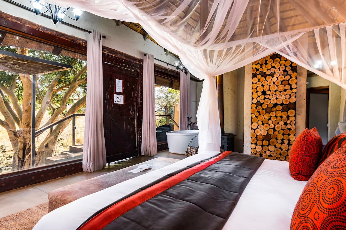 Un dormitorio con una cama grande, una pared de troncos de madera y vistas a árboles a través de la ventana.