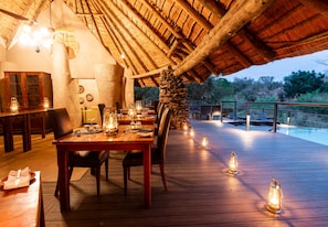 An outdoor dining area with a wooden deck, stone pillar, and lanterns.
