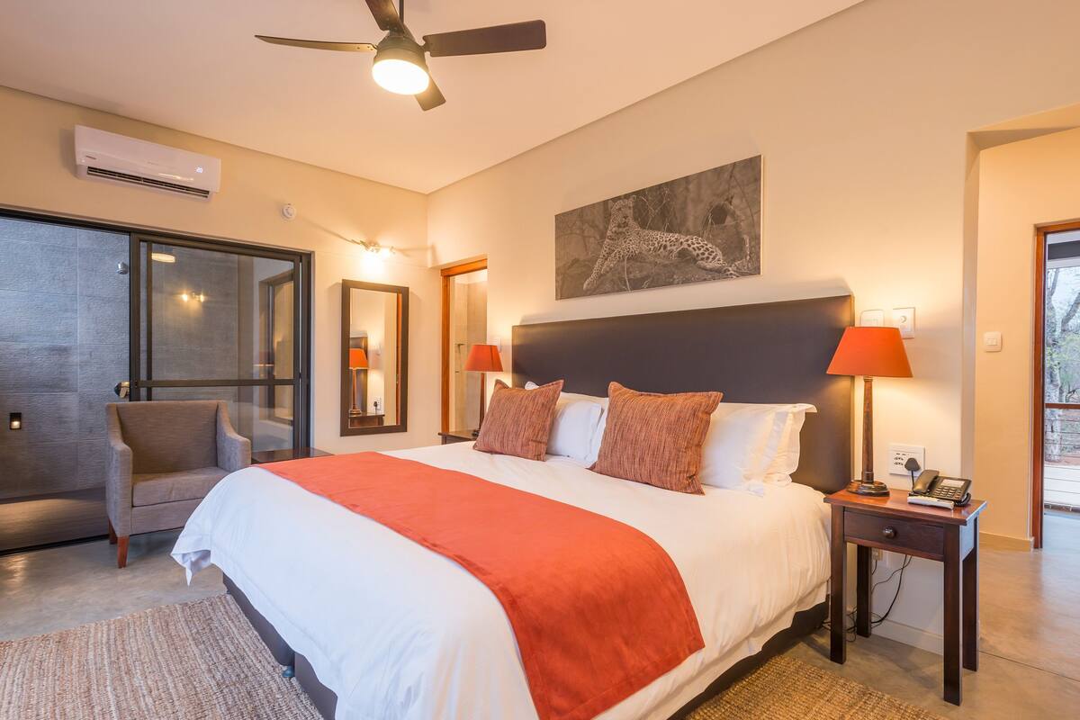 Un dormitorio con cama, una silla, un escritorio, una lámpara y un ventilador de techo.