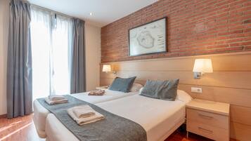 Habitación de hotel con dos camas, un muro de ladrillo y un cuadro enmarcado.