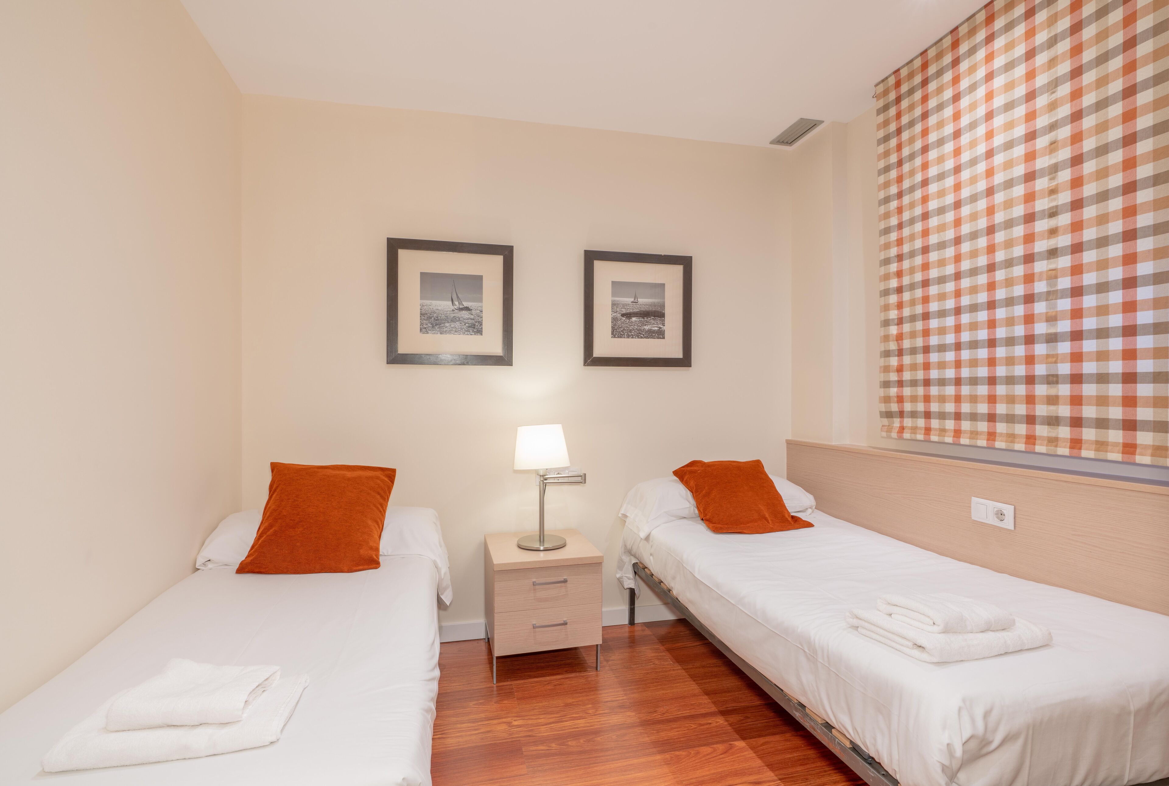 Une chambre d’hôtel avec deux lits simples, une table de chevet avec une lampe et une fenêtre avec des rideaux à carreaux.