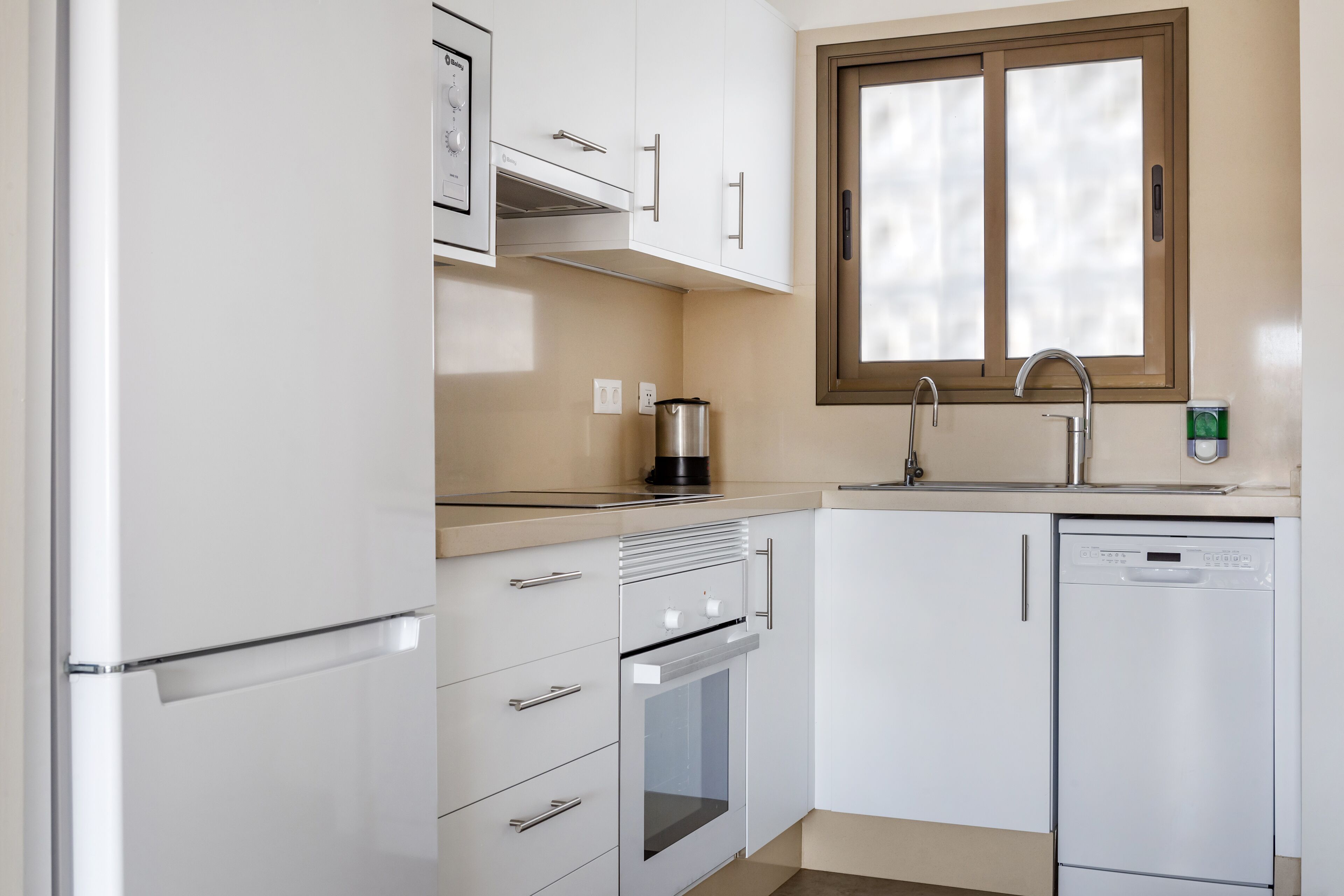 A compact kitchen with white cabinetry, a built-in oven, a coffee maker, and a dishwasher.