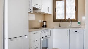 A compact kitchen with white cabinetry, a built-in oven, a coffee maker, and a dishwasher.
