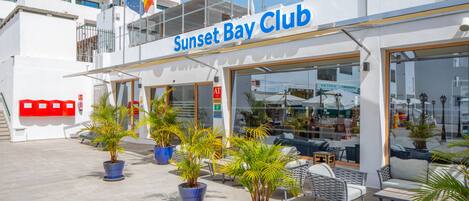 Exterior del Sunset Bay Club con asientos al aire libre y plantas en macetas.