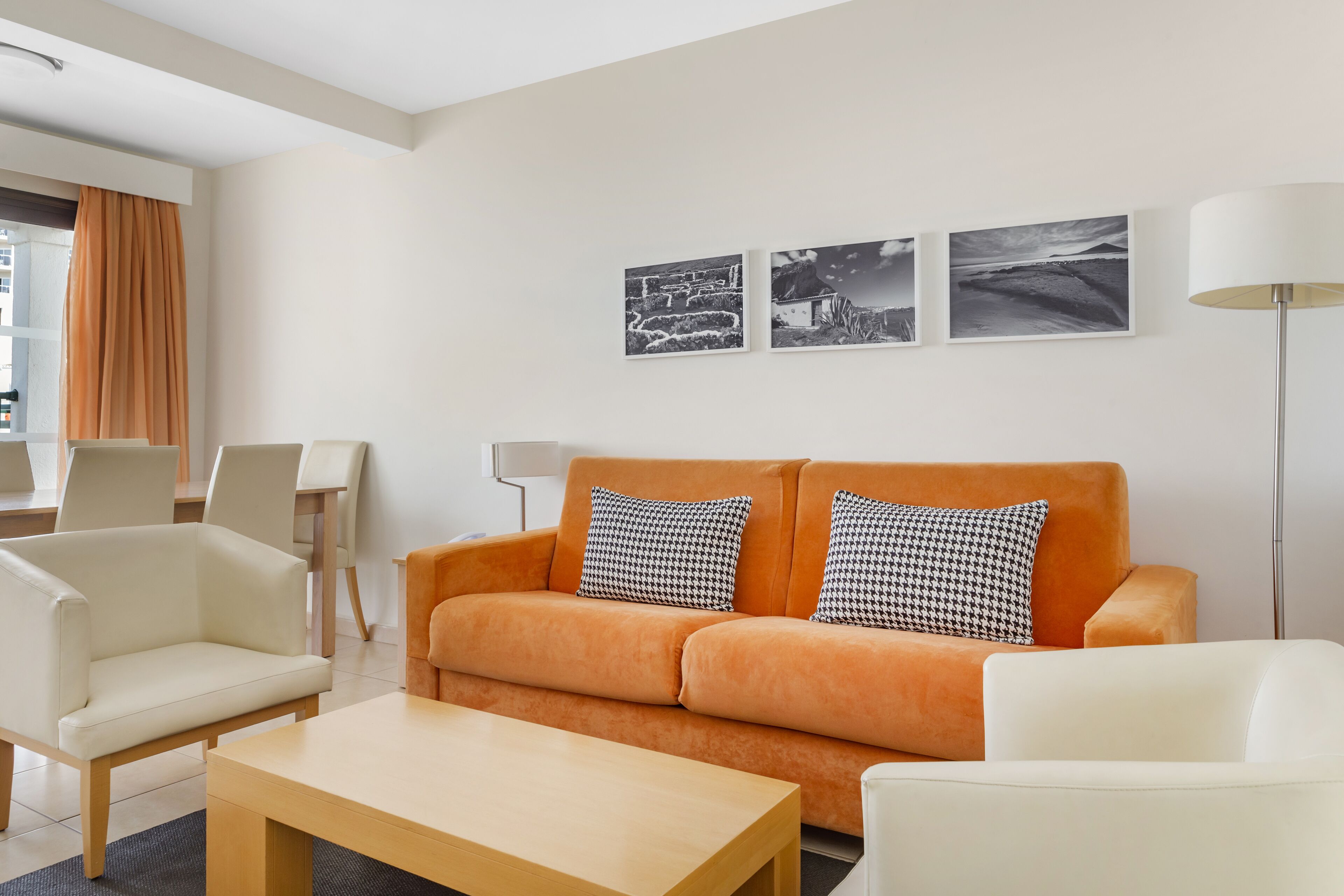 A modern living room with a sofa, two armchairs, a coffee table, and a floor lamp. There are three black and white photographs on the wall.