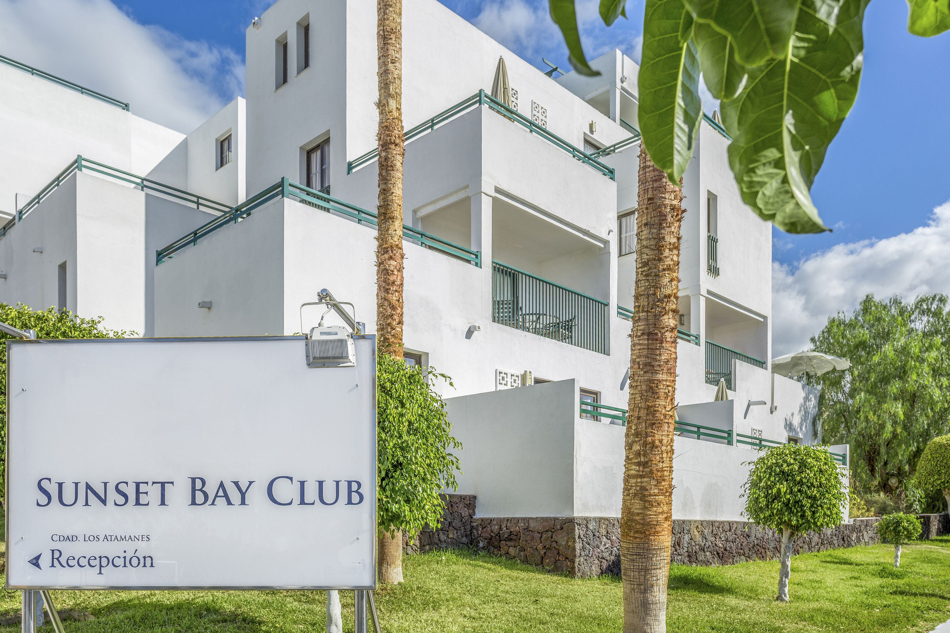 A white building with balconies and a sign reading "Sunset Bay Club."