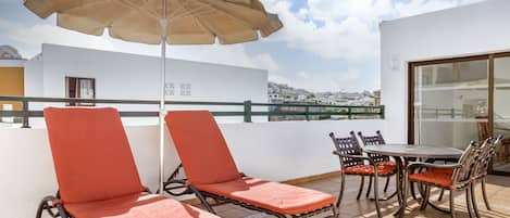 A terrace with two lounge chairs, a table, and chairs, an umbrella, and a view of the city.