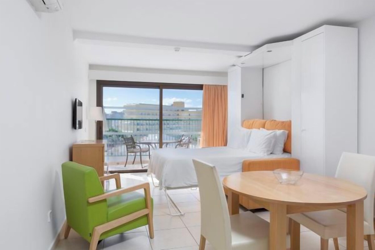 A hotel room with a bed, a balcony, a dining table, and a chair.