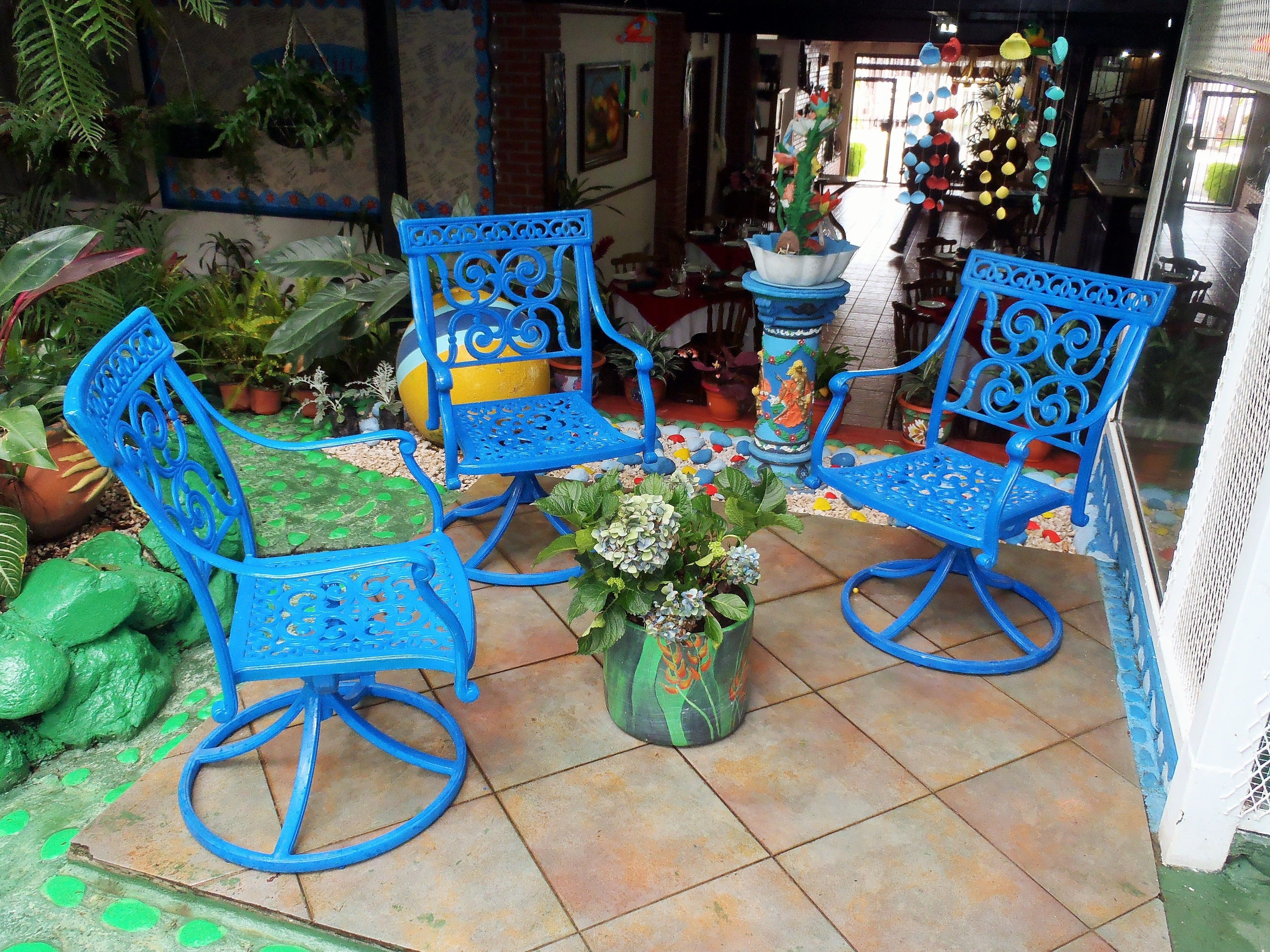 Un patio con sillas y mesa de metal azul, rodeado de macetas y elementos decorativos.