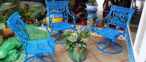 Un patio con sillas y mesa de metal azul, rodeado de macetas y elementos decorativos.