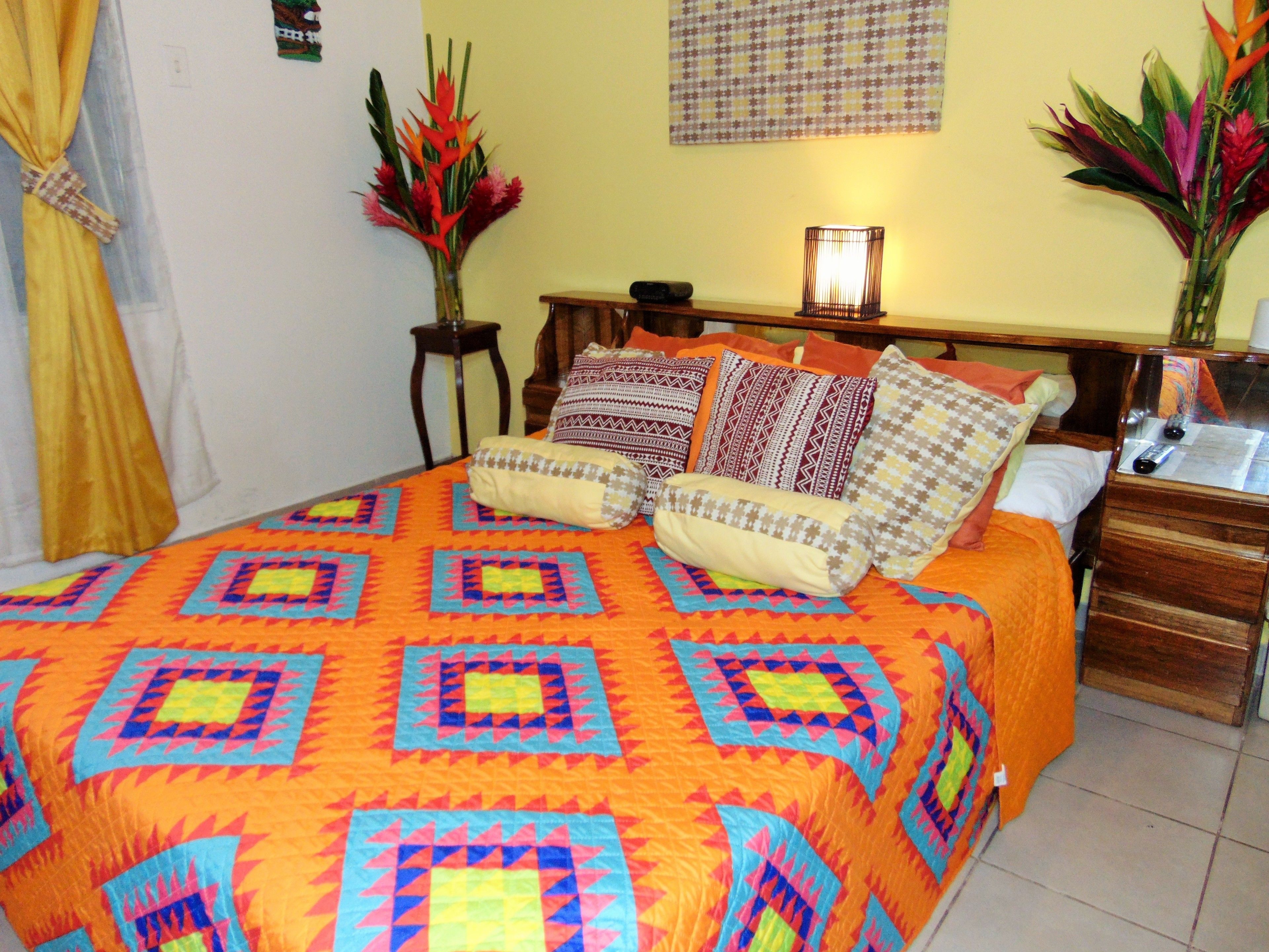 A bed with a colorful quilt, a bedside table with a lamp, and decorative plants.