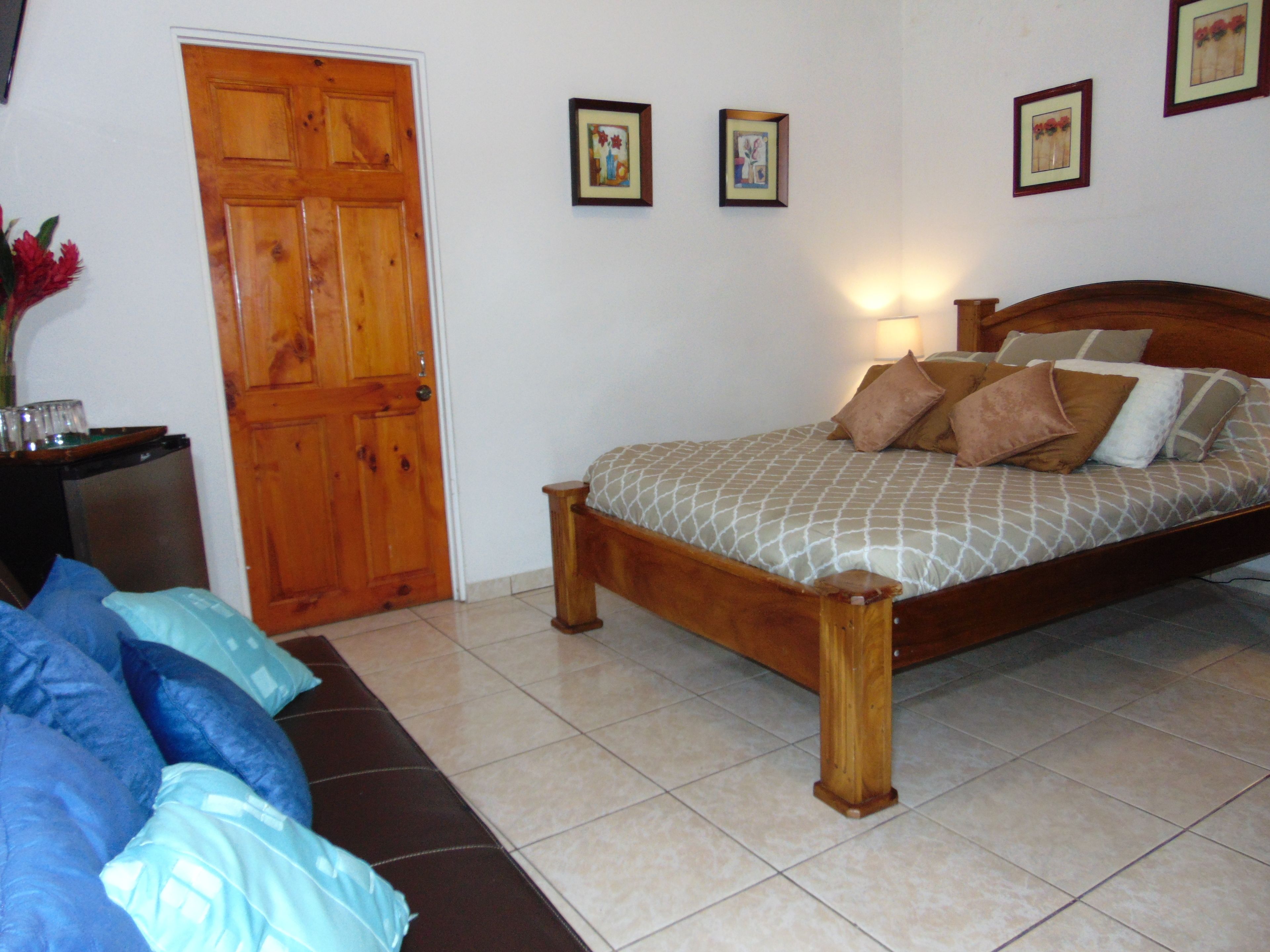 A bedroom with a wooden bed, a nightstand, a blue sofa, and a wooden door.