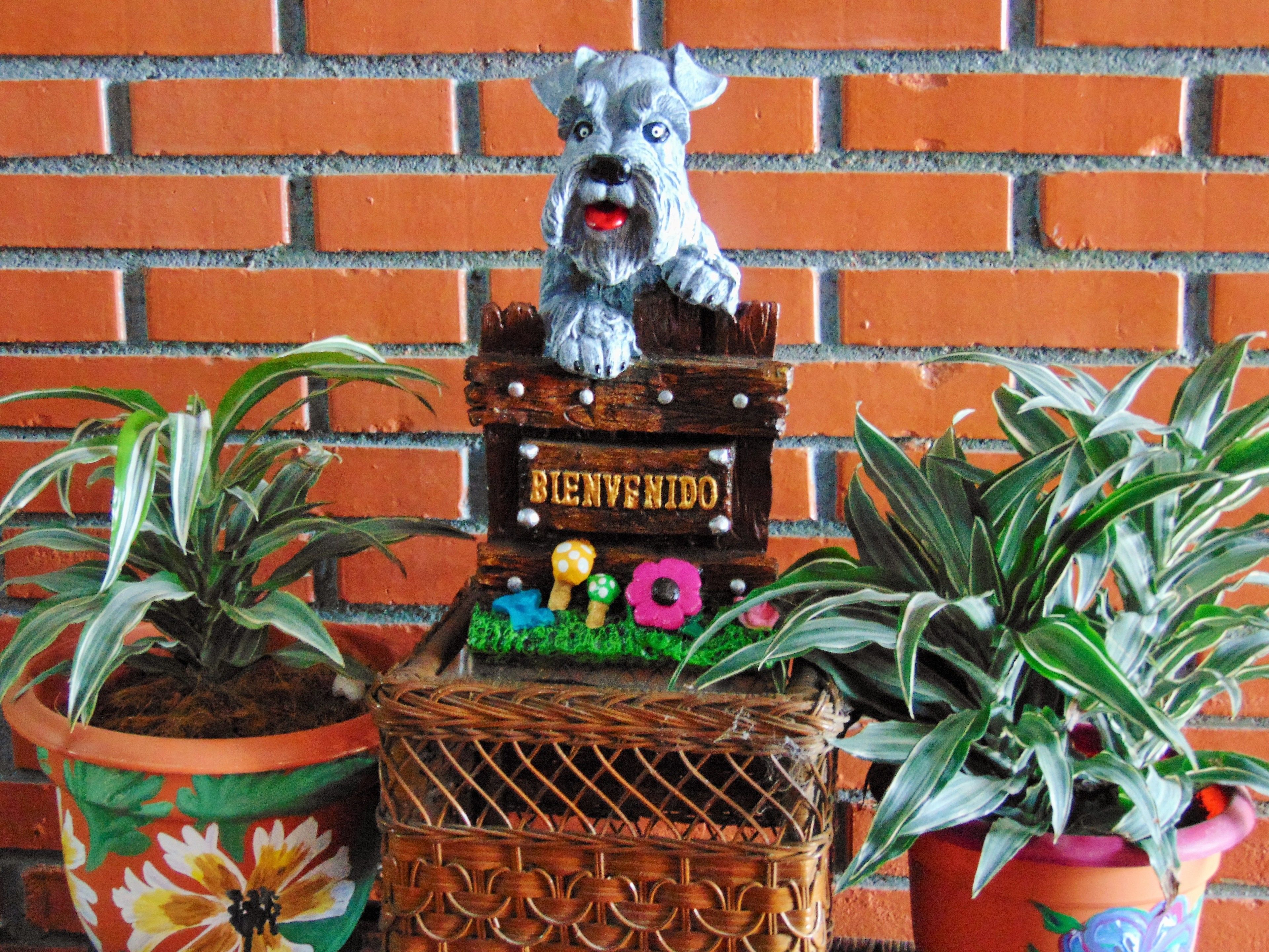 Ein Willkommensschild mit einer Hundefigur, umgeben von Blumentöpfen.