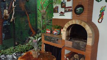 Un interior rústico con chimenea de ladrillo, una mesa de madera y diversos objetos decorativos, incluyendo una jaula de pájaros y adornos en la pared.