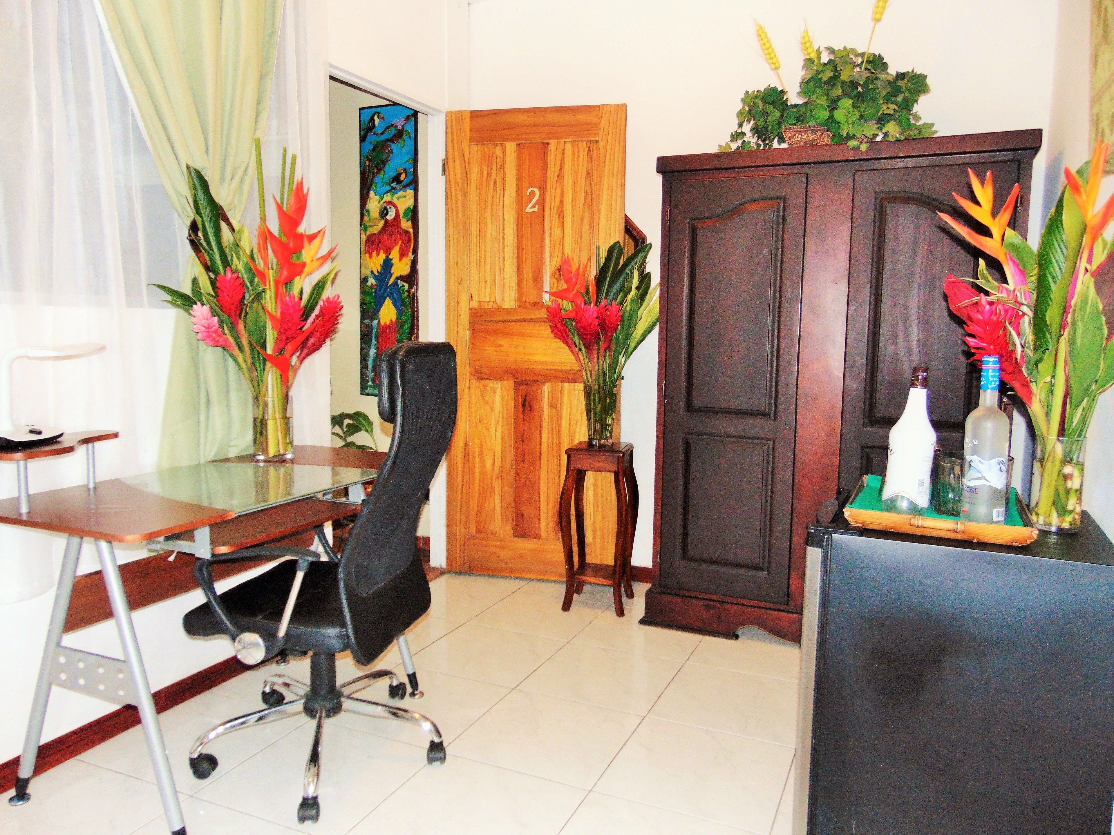 Un salón de conferencias con una puerta de madera, un escritorio con una silla y dos jarrones con flores rojas.