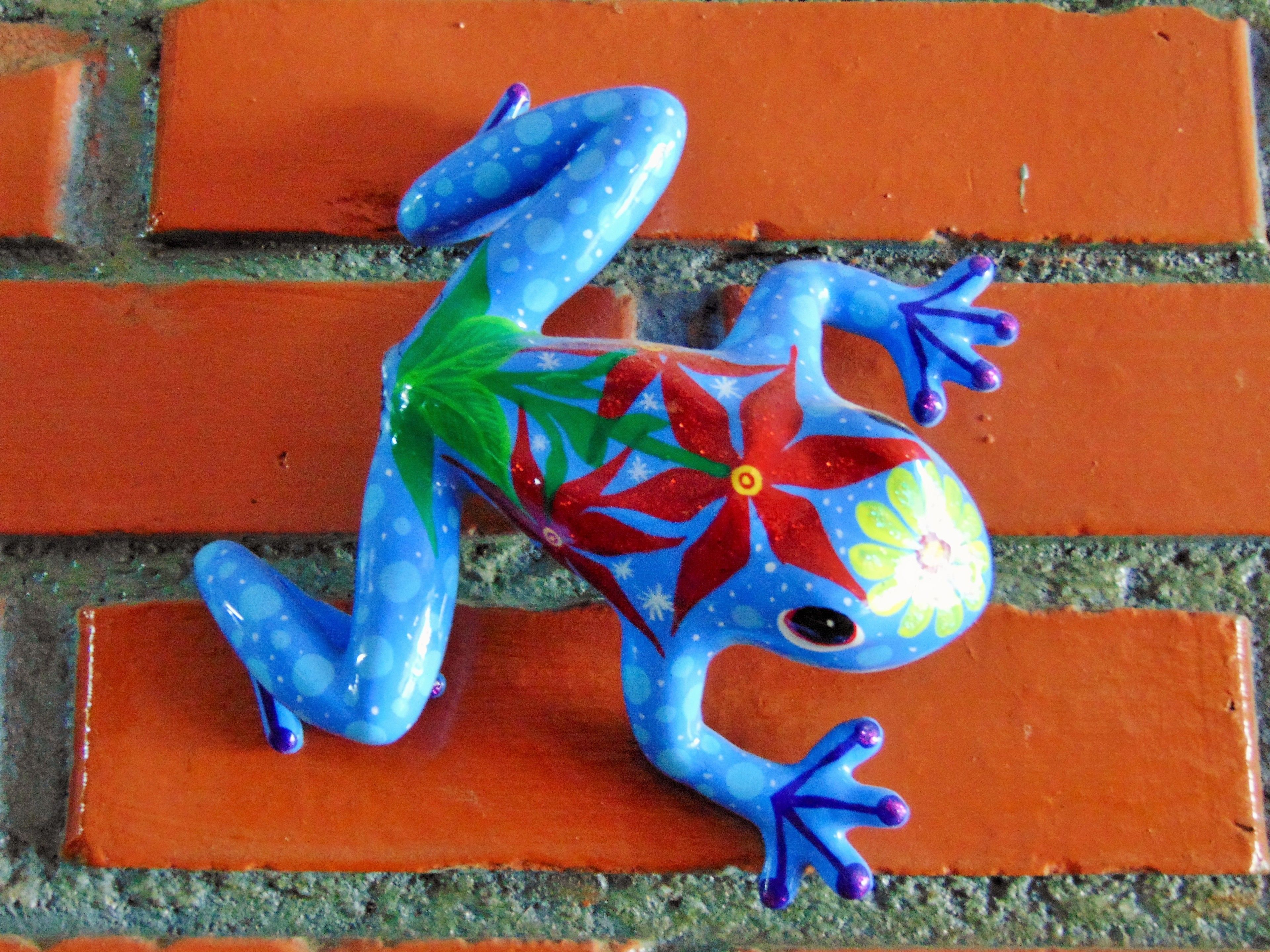 A colorful frog sculpture on a brick wall.